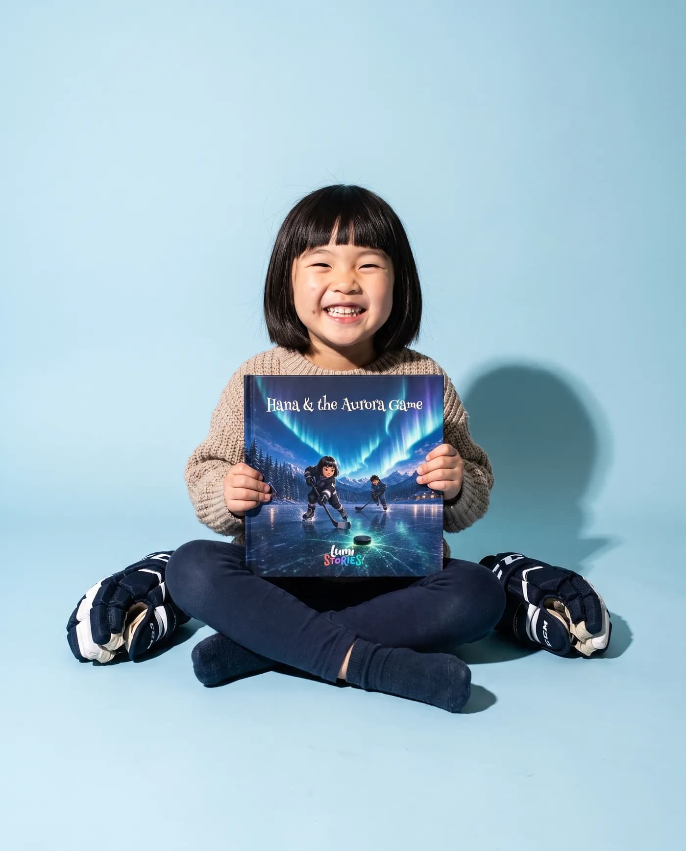 A girl sits cross-legged on a sky-blue backdrop holding her own copy